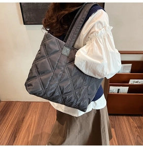 Detail of grey quilted nylon tote bag with rhombus embroidery on model in a cozy room