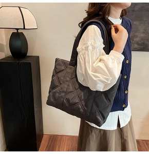 Deep grey quilted tote bag with diamond stitching shown on a model in a minimal room