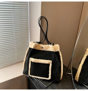 Close-up of black suede tote bag featuring white faux shearling trim and leather handles