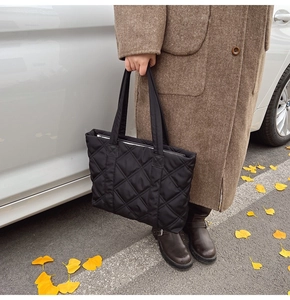 Outdoor shot of a black quilted nylon tote bag with rhombus embroidery and metal zipper