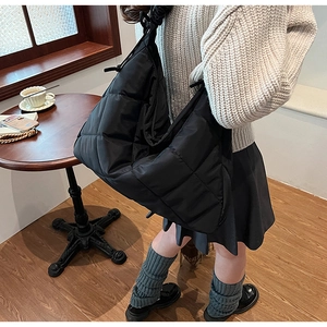 Side view of a large black quilted nylon tote bag worn over the shoulder for daily use