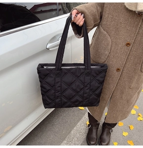 Borsa tote nera trapuntata a rombi con tracolla in nylon mostrata in ambiente esterno