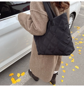 Close-up of black quilted nylon tote bag worn with a brown tweed coat in autumn