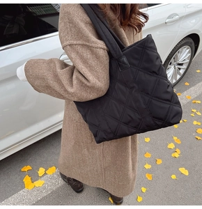 Close-up of black quilted nylon tote bag with rhombus embroidery in an autumn street setting