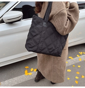 Detail of black quilted nylon tote bag featuring diamond embroidery on an autumn street