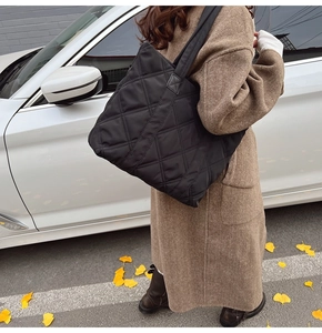 Woman in brown coat carrying a large black quilted nylon tote bag in autumn street