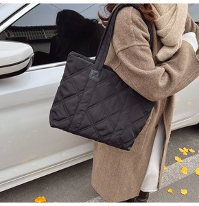 Close-up of a large black quilted nylon tote bag with rhombic embroidery and shoulder strap
