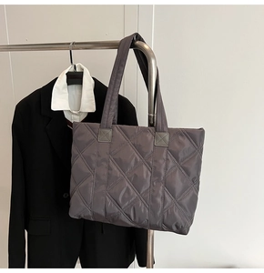 Detail of dark grey quilted nylon tote bag showing diamond embroidery and wide handle