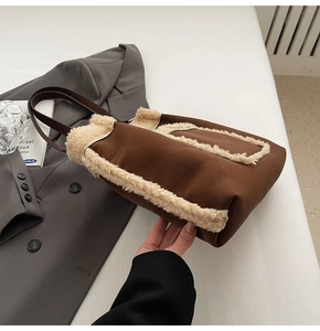 Detail of a brown faux suede tote bag with plush beige fur trim on a gray suit jacket
