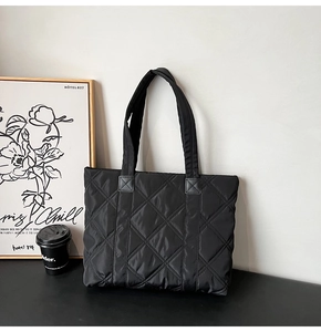 Black quilted nylon tote bag with rhombus patterns next to a coffee cup