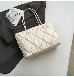 Detail of cream white quilted tote bag with soft diamond stitching on a grey blazer