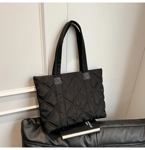 Detail of black quilted nylon tote bag showing diamond stitch pattern and handle reinforcement