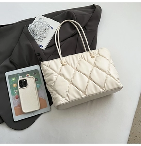 Close-up of cream quilted puffer tote bag with soft diamond stitching and laptop props