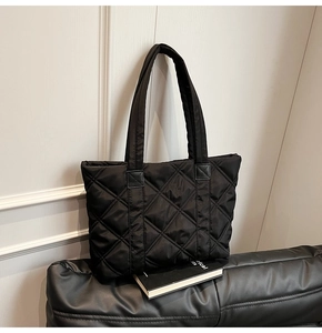 Detail of black quilted nylon tote bag with rhombic embroidery on a leather sofa