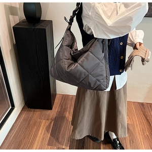 Detail of dark grey quilted nylon tote bag with pleated strap worn by a female model