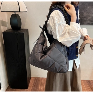 Close-up of a large grey quilted nylon tote bag with pleated straps on a female model