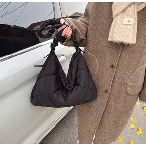 Detail of black quilted nylon bag featuring pleated handle and diamond lattice texture