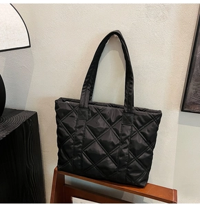 Close-up of black quilted nylon tote bag with rhombus embroidery on wooden shelf