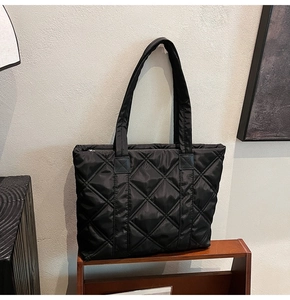 Macro view of black quilted nylon tote bag showing glossy texture and diamond stitching
