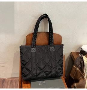 Detailed view of black quilted nylon tote bag with reinforced handles on vintage chair