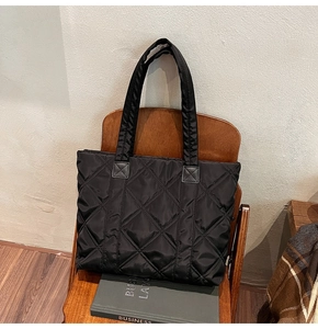 Detail of black quilted nylon tote bag with rhombus patterns on a wooden chair