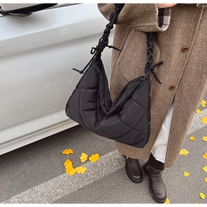 Detail of black quilted tote bag with ruched shoulder strap and decorative tie knots
