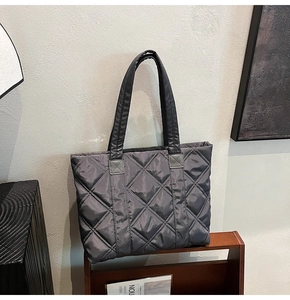 Detail showing deep gray quilted nylon tote bag with large diamond stitch on wood shelf
