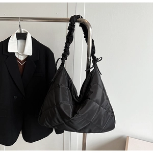 Detail of black quilted tote bag with ruched shoulder strap and delicate bow decoration
