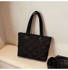 Detailed view of black quilted nylon tote bag with large diamond stitching on a bench