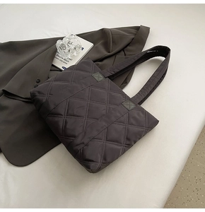 Detail of grey quilted nylon tote bag with rhombus embroidery on a formal suit backdrop