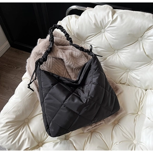 Detail of black quilted nylon bag with ruched strap and side drawstring on white sofa