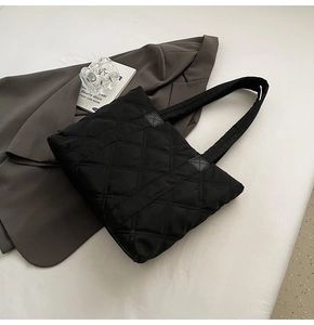 Close-up of black quilted nylon tote bag with rhombus embroidery on a gray blazer