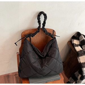 Black quilted tote bag with ruffled scrunchie strap and bow detail on a vintage chair