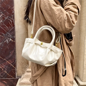 Glossy white pleated hobo handbag with gold clasp worn over a stylish trench coat