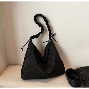 Detail of black quilted nylon tote bag featuring ruffled shoulder straps and side ties