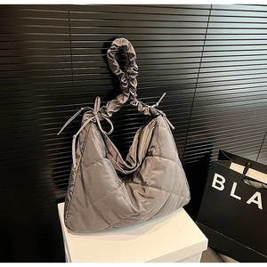 Close-up of gray quilted nylon bag with pleated strap and bow detail on display