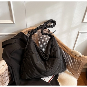 Detail of black quilted nylon bag featuring ruffle strap and elegant knot on vintage chair