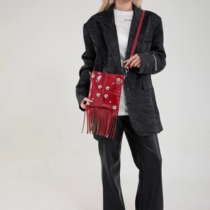 Red patent leather crossbody bag with silver studs and long tassels on a model
