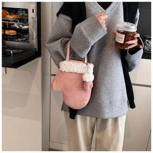 Pink mitten-shaped plush handbag with white faux fur trim held in a kitchen setting
