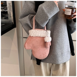 Macro detail of a pink suede mitten-shaped crossbody bag with white faux fur trim and pom-pom