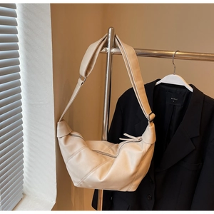 Detailed view of cream-colored crescent bag with stitching and wide shoulder strap