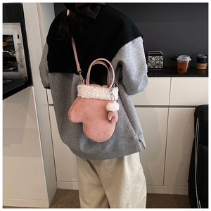Detail view of pink glove-shaped crossbody bag with white faux fur trim and mini charm