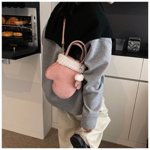 Pink glove-shaped crossbody bag with white faux fur trim and pom-pom detail on model