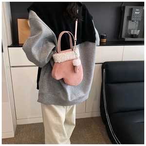 Detail of pink glove-shaped crossbody bag featuring plush white trim and a fuzzy pom-pom