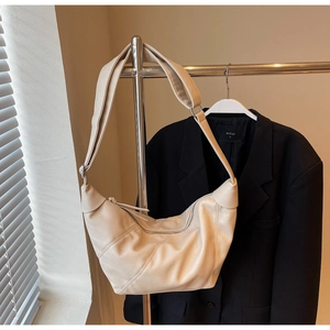Detail of a beige crescent dumpling bag with lychee leather texture on a metal stand
