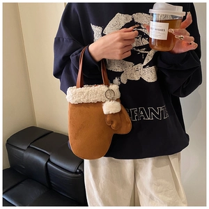 Detail of a brown suede glove-shaped handbag with white faux fur trim and pompom charm