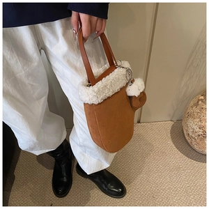 Detail of brown suede bucket bag featuring white faux fur trim and heart charm