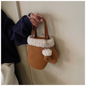 Detail of creative mitten-shaped brown suede handbag with white faux fur trim and pompom