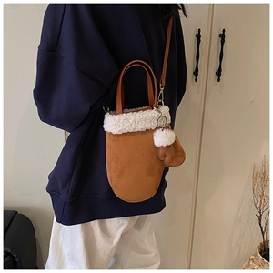 Detail of brown suede glove-shaped crossbody bag with white faux fur trim and mini charm