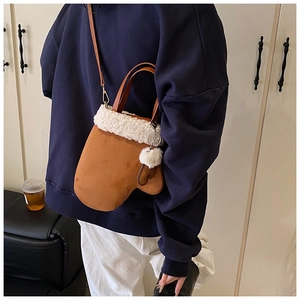 Brown glove-shaped crossbody bag with white fleece trim and pompom detail on model